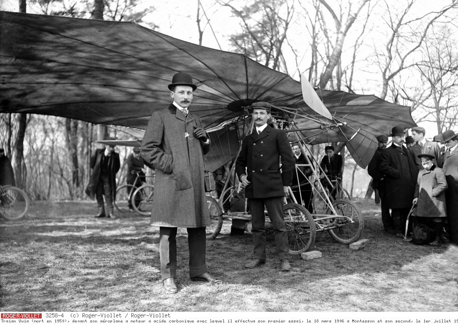 Traian Vuia (mort en 1950), devant son aéroplane à moteur à acide carbonique avec lequel il effectua son premier essai, le 18 mars 1906 à Montesson et son second, le 1er juillet 1906 à Issy-les-Moulineaux. A gauche : Delagrange. (Photo probablement prise en 1907).